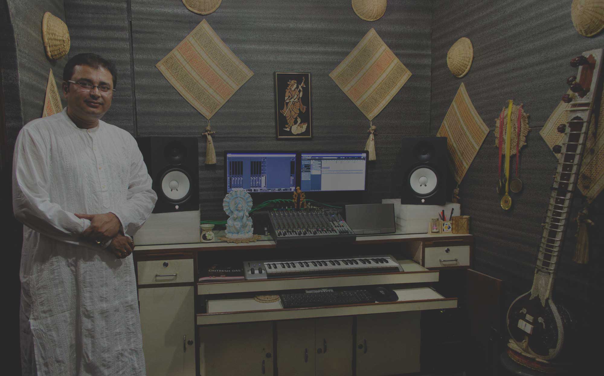 Jayanta Banerjee standing beside the mixing desk in his recording studio in Kolkata, with a sitar against the wall